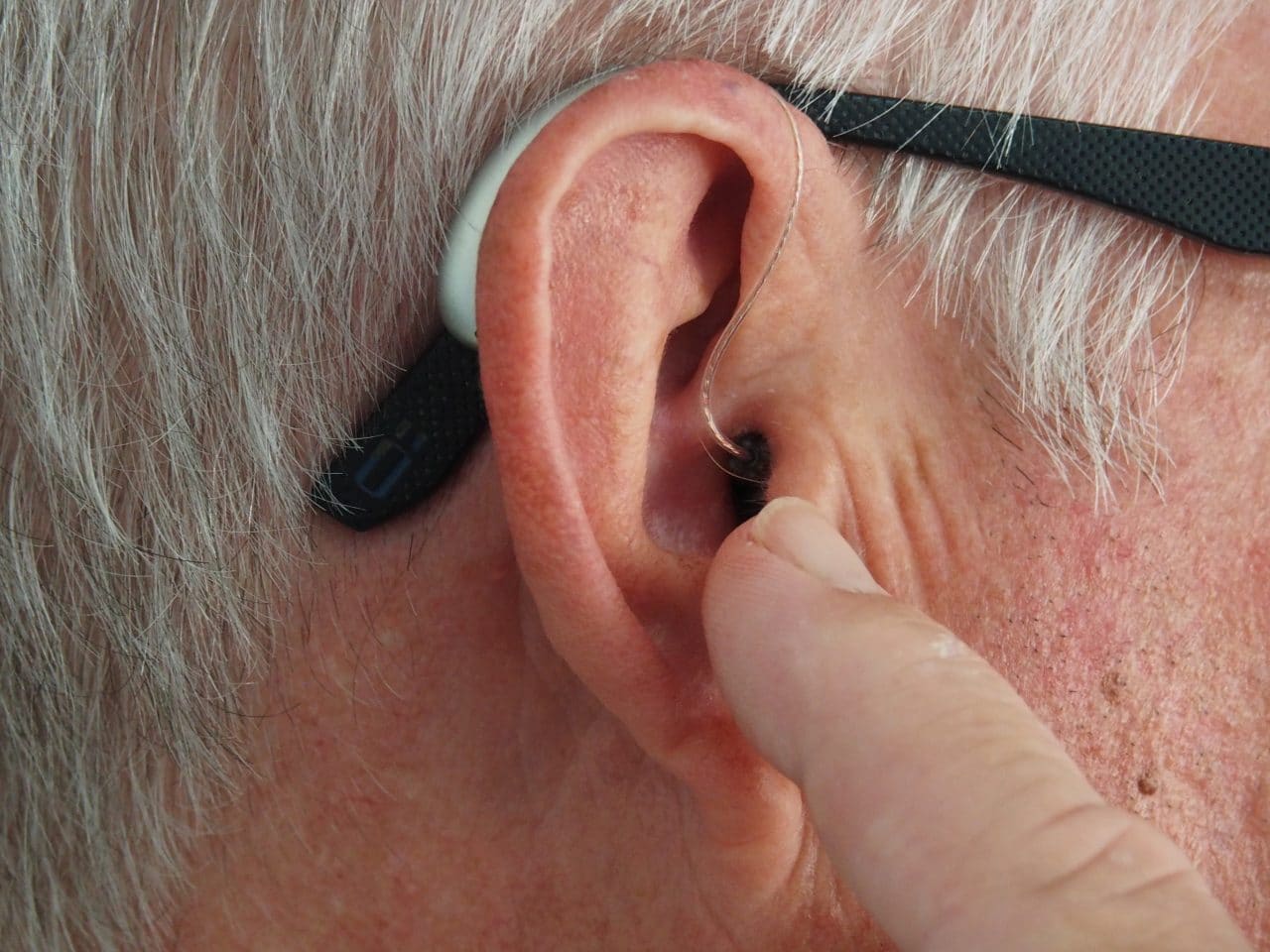 Hearing Aids Vs. Cochlear Implants: What Are the Benefits? Man points at his hearing aid