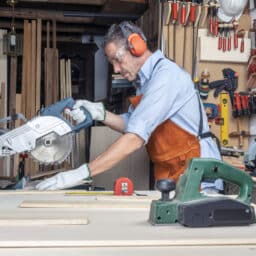 Man wearing earmuffs using a rotary saw in his woodshop