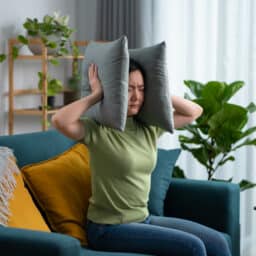 Woman putting pillows around her ears to drown out music ear