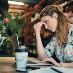 Stressed woman holding the bridge of her nose while looking at her laptop