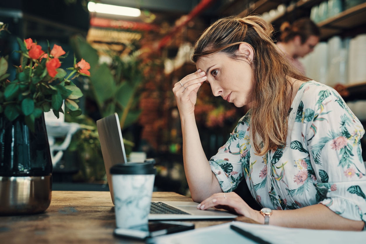 Stressed woman holding the bridge of her nose while looking at her laptop.
