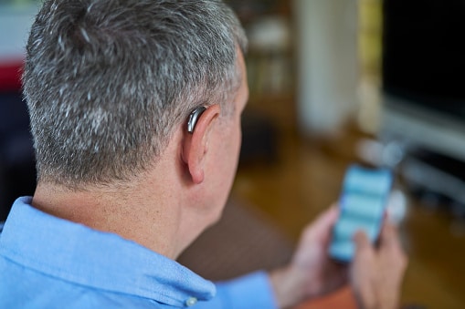Close Up Of a Man Wearing Wireless Hearing Aid Using Mobile Phone  At Home