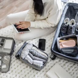 A woman in white clothes uses a tablet to check in for an airplane flight before leaving for the airport.